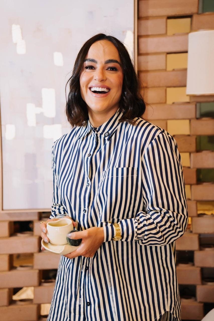 Camila Meneses sorrindo, com uma xícara nas mãos